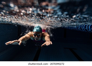 Dark blue water, depth. Underwater view of swimming movements details. One female swimmer in swimming cap and goggles training at pool. Healthy lifestyle, power, energy, sports movement concept. - Powered by Shutterstock