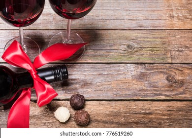 A dark bottle of wine with a red bow, glasses of wine and chocolate truffles.Top view