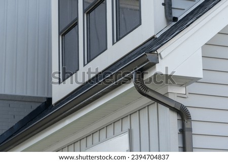 Dark brown gutter guard system, fascia, drip edge, soffit, downspout strap with white vinyl horizontal siding at a luxury American single family home neighborhood USA	