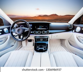 Dark Car Interior - Steering Wheel, Shift Lever And Dashboard. Car Modern Inside. Front View On Sunset And Sea Background. The Sun Shines In The Glass.glare