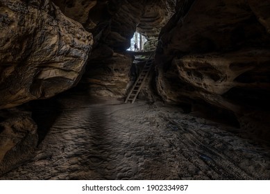 Dark cave feature with sandy floor, ladder and lone female explorer  - Powered by Shutterstock