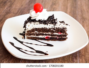 Dark Chocolate Cake Topping With Cherry And Whipping Cream Placed On Wood Background