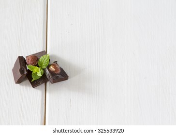 Dark chocolate with mint leaf with nuts on a wooden background white
