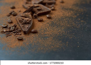Dark chocolate stack, chips and cocoa powder with coffee beans on a dark background. Confectionery and food concept. Top view, copy space, selective focus..