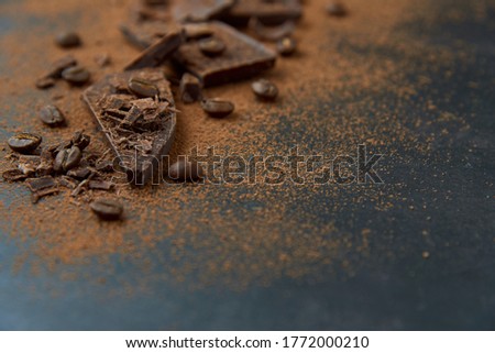 Dark chocolate stack, chips and cocoa powder with coffee beans on a dark background. Confectionery and food concept. Top view, copy space, selective focus..