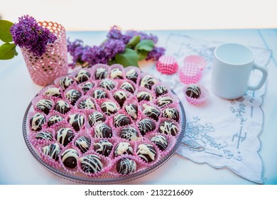 Dark Chocolate Truffle Dessert On Big Plate Decorated With White Glazed. Vegan Raw Cookies Served With Violet Lilac Flowers. Above Close Up View