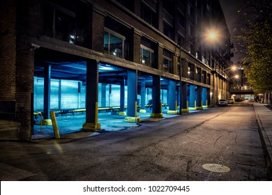 Dark City Downtown Street Road And Alley At Night With An Industrial Warehouse Loading Dock.