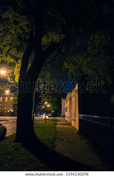 Dark city street\
sidewalk with tree at\
night