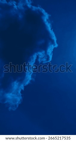 A dark cloud edge curls into the deep blue sky like a silent wave or sleeping creature, evoking a sense of cosmic mystery and surreal minimalism.