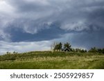 Dark cloud over green grassy hill in Spring. Funnel cloud forming overflow hill. Dark clouds in circular form.