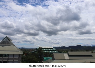 Dark clouds cover the blue sky above the green roofs of the buildings surrounded with mountainous area. 