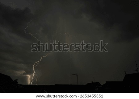 Dark clouds gather as lightning strikes illuminate the night over rooftops. The intense storm brings thunder and rain to the quiet neighborhood below. Bas rhin, Alsace, grand est, France, Europe.