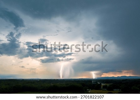 Dark clouds gather as lightning strikes illuminate distant mountains fields during summer thunderstorm.