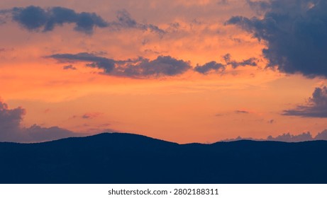 Dark clouds gliding over the mountain range at twilight. The magnificent harmony of the warm orange and yellow hues covering the sky.
