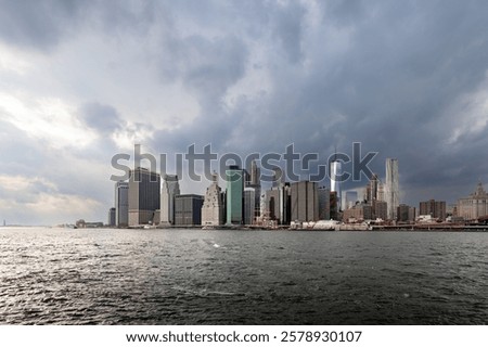Dark clouds loom over Downtown Manhattan, highlighting modern architecture in Financial District during an overcast day.