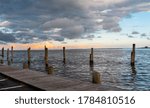 Dark clouds rolling in with orange clouds from the sun setting in the distance by a pier in the Great South Bay.