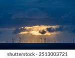 Dark clouds of a thunderstorm with rain falling onto the north sea with silhouettes of wind turbines in the background