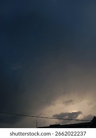 Dark cloudy sky with soft sunlight peeking through the clouds during late afternoon. Captured in a residential area with silhouette of rooftops. A natural atmospheric scene.