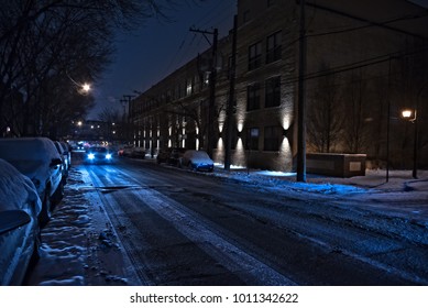 Dark And Cold Chicago Winter Street With Snow And Ice And An Oncoming Car At Night.