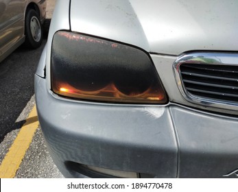 Dark Colored Plastic Car Headlight Torn And Damaged. Headlamp Tint Able To Prevent The Headlamp From Turning Into Yellowish, Protect The Headlamp From Stone Chips And Refine The Appearance Of The Car.