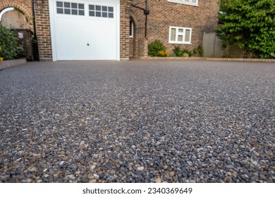 A dark coloured resin driveway at the front of a detached residential property
