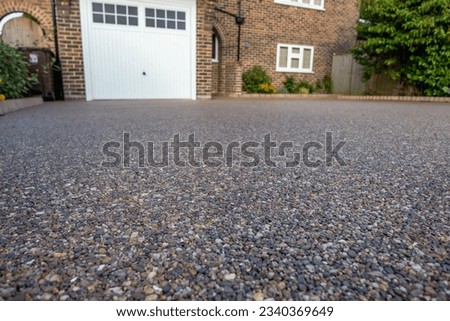 A dark coloured resin driveway at the front of a detached residential property
