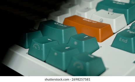 Dark composition of mechanical keyboard highlighting orange Enter and green Shift keys, focused on front keys with background fading into black shadow.