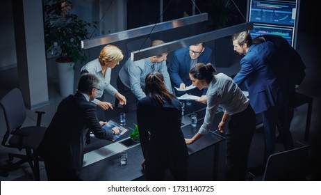 In the Dark Corporate Meeting Room Diverse Group of Executives, Business Associates and Investors Lean on a Conference Table During Emotional Discussion, Planning and Strategizing. High Angle Shot