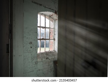 Dark And Creepy Wooden Cellar Window In Abandoned Workhouse Viewed Through Open Door Bright Sun Light Rays Shining Through On Wall In Scary Sinister Abandoned Basement Room. Atmospheric Moody Room.