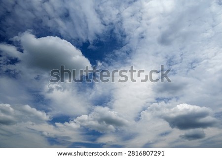 dark cumulus cloud located on the left side of the frame against volumetric white clouds and a bright blue sky