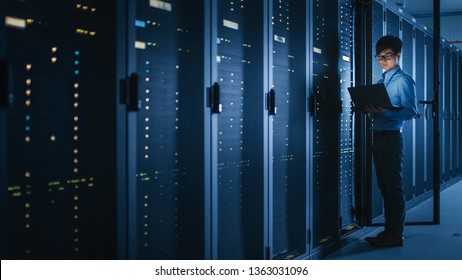 In Dark Data Center: Male IT Specialist Stands Beside the Row of Operational Server Racks, Uses Laptop for Maintenance. Concept for Cloud Computing, Artificial Intelligence, Cybersecurity. - Powered by Shutterstock