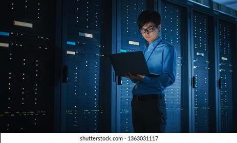 In Dark Data Center: Male IT Specialist Walks along the Row of Operational Server Racks, Uses Laptop for Maintenance. Concept for Cloud Computing, Artificial Intelligence, Supercomputer, Cybersecurity