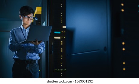 In Dark Data Center: Male IT Specialist Stands Beside the Row of Operational Server Racks, Uses Laptop for Maintenance. Concept for Cloud Computing, Artificial Intelligence, Supercomputer. Neon Lights