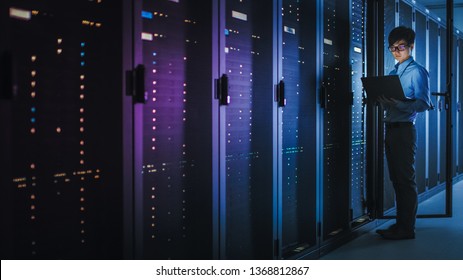 In Dark Data Center: Male IT Specialist Stands Beside the Row of Operational Server Racks, Uses Laptop for Maintenance. Concept for Cloud Computing, Artificial Intelligence, Supercomputer. Neon Lights