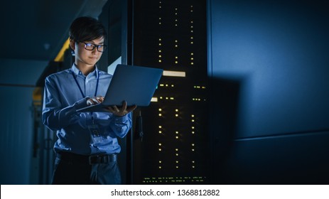 In Dark Data Center: Male IT Specialist Stands Beside the Row of Operational Server Racks, Uses Laptop for Maintenance. Concept for Cloud Computing, Artificial Intelligence, Supercomputer. Neon Light