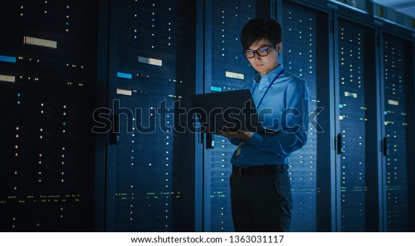 In Dark Data Center: Male IT Specialist\
Walks along the Row of Operational Server Racks, Uses Laptop for\
Maintenance. Concept for Cloud Computing, Artificial Intelligence,\
Supercomputer, Cybersecurity