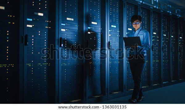 In Dark Data Center: Male IT Specialist\
Walks along the Row of Operational Server Racks, Uses Laptop for\
Maintenance. Concept for Cloud Computing, Artificial Intelligence,\
Supercomputer, Cybersecurity