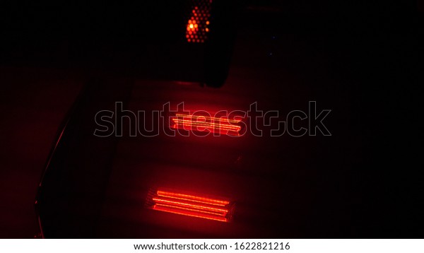 In the dark, detail of the car body is\
drying under the lamps after painting. red lamps for drying painted\
parts are switched on in the service\
station.