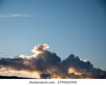 Dark dramatic clouds lit by warm sunset light stretch across a clear blue sky, creating a serene natural weather scene with wide open space.