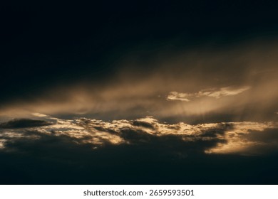 Dark and dramatic clouds roll across the sky, softly backlit by the fading golden sun, evoking a sense of wonder and tranquility.