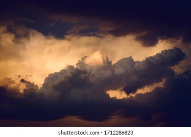 Dark, dramatic nimbus clouds at sunset, lit by the last rays of sunlight before a storm.