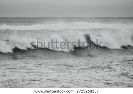 Dark and dramatic ocean waves under a stormy grey sky, moody coastal landscape.
