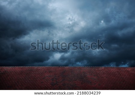 Dark Dramatic Sky before Rain and Storm. Cyclone is coming with Black Windy Cloud. House Cover by Red Tiles Roof as foreground. Weather and Season Change
