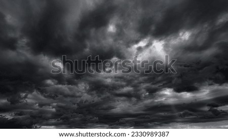 dark dramatic sky with black stormy clouds before rain or snow as abstract background, extreme weather, the sun shines through the clouds, high contrast photo
