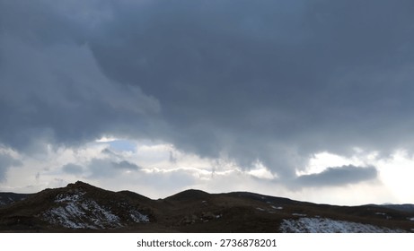 Dark dramatic storm clouds forming over a remote mountain landscape, creating a moody and atmospheric nature scene.