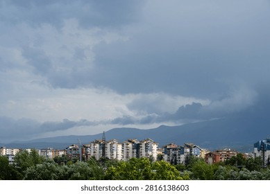 Dark dramatic storm clouds looming over residential city buildings and distant mountains