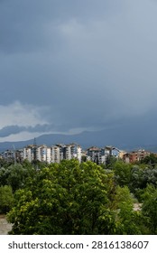 Dark dramatic storm clouds looming over residential city buildings and distant mountains