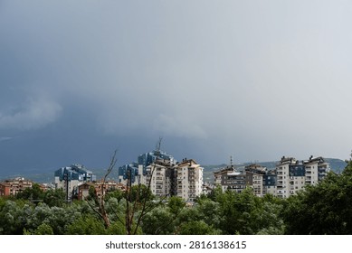Dark dramatic storm clouds looming over residential city buildings and distant mountains