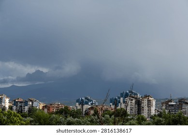 Dark dramatic storm clouds looming over residential city buildings and distant mountains
