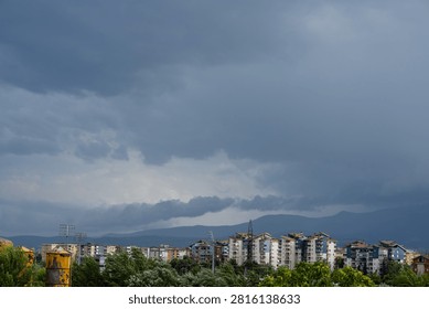 Dark dramatic storm clouds looming over residential city buildings and distant mountains